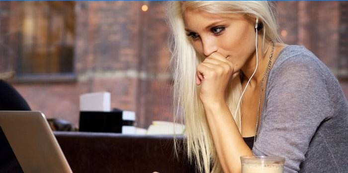 Mergina sėdi prie nešiojamojo kompiuterio ausinėse