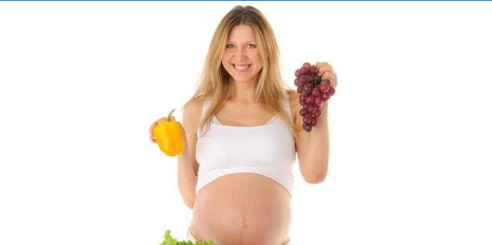 Nėščia moteris rankose laiko pipirus ir vynuogių krūvą