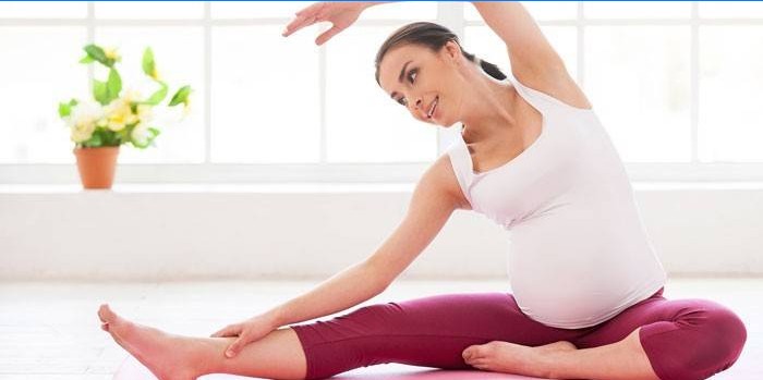 Nėščia moteris pratimą atlieka sėdėdama ant grindų