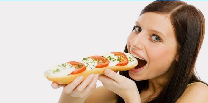 Mergaitė valgo sumuštinį su pomidorais ir sūriu