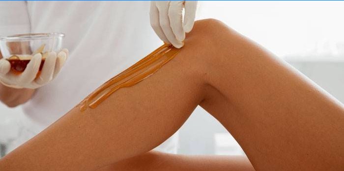 Kosmetologė depiliacijai deda pastą ant kojų odos.