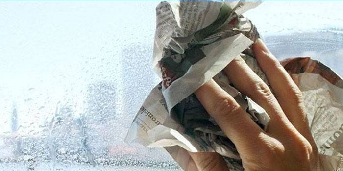 Žmogus trina lango stiklą su laikraščiu